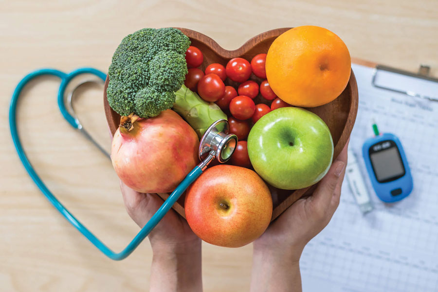 Two hands holding a bowl of fruit and vegetables with diabetes-related equipment in the background.