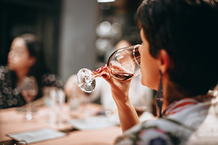 A women lifting a glass of wine to her lips to take a drink while out with friends