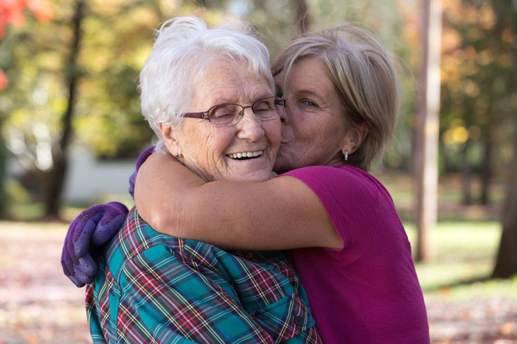 Elderly mother and daughter hugging outside.
