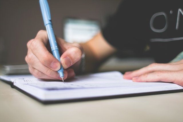 close up of a males hand holding a blue pen writing in a notebook