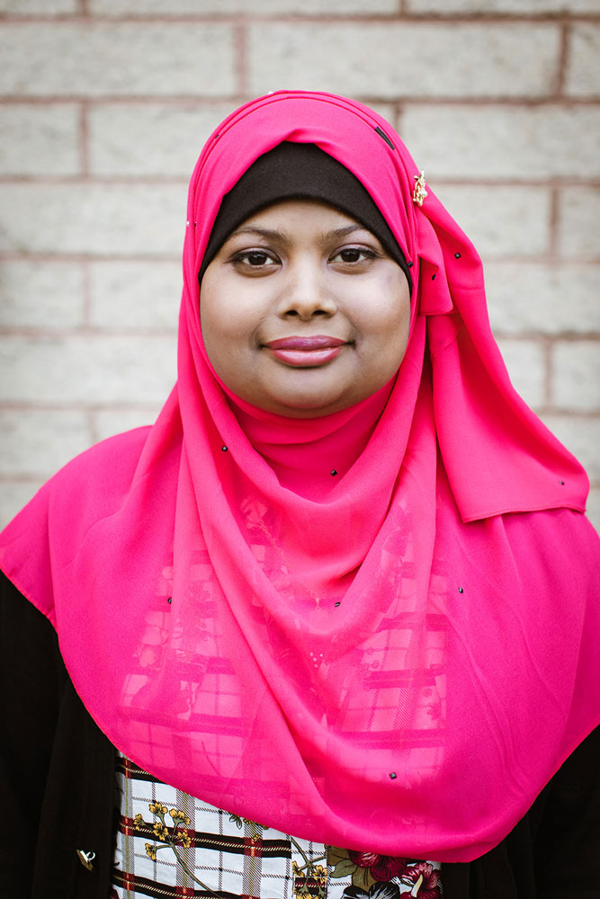 A woman wearing a pink headscarf smiles at the camera.