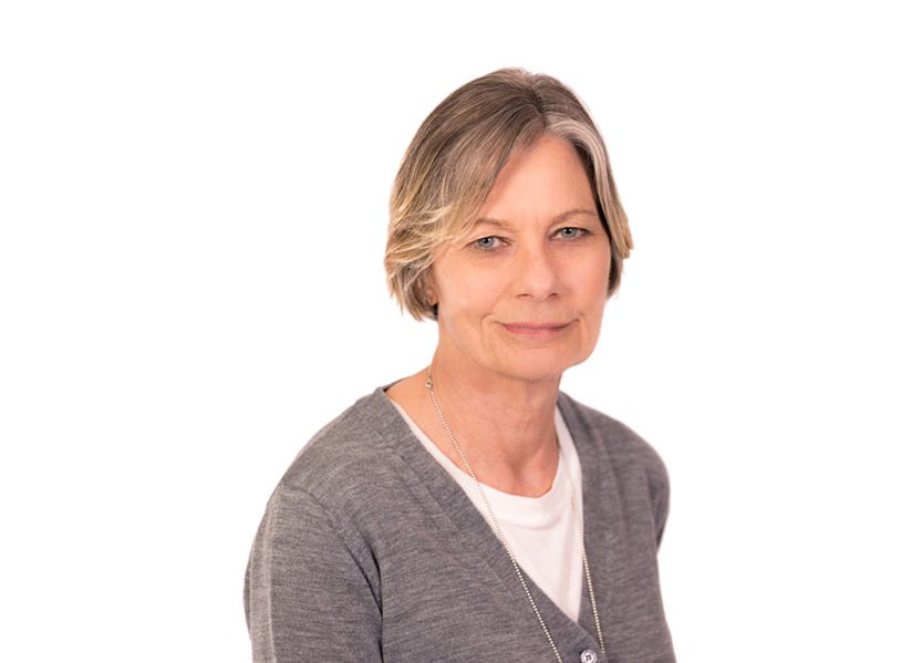 Joanne Headshot of board member Joanne Booth, smiling with short hair, wearing a grey cardigan over a white t-shirt and a long silver necklace