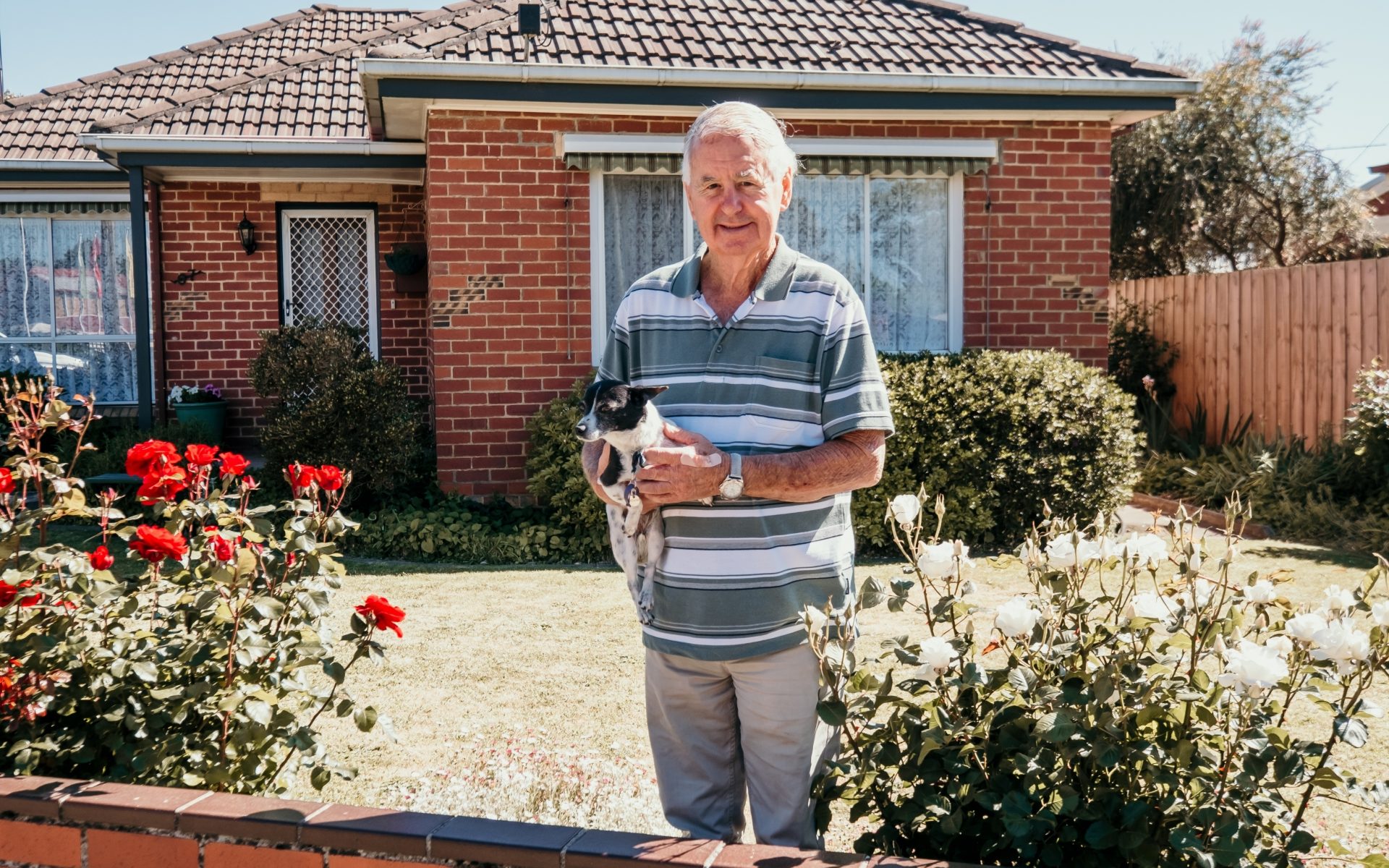 Seniors (18) man standing in front of a house, holding a small dog