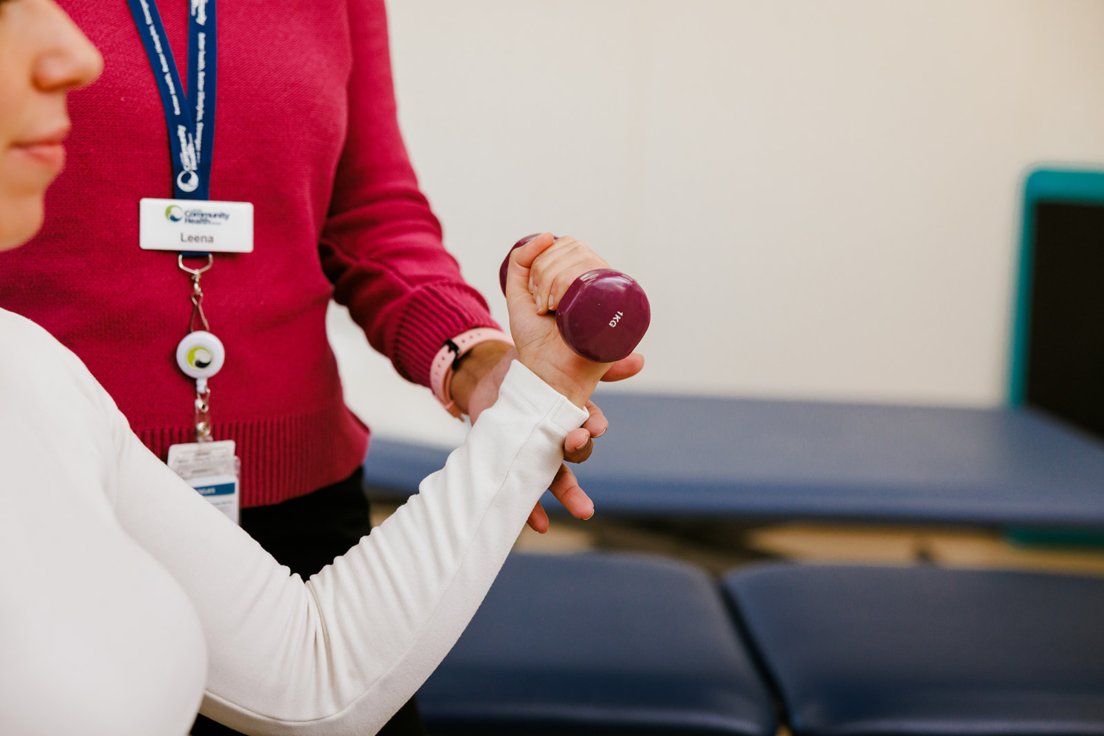 exercise physiologist helping a person lift a hand weight 